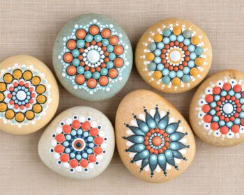 Sechs bemalte Kieselsteine mit bunten Punktmandalas in Türkis, Orange und Weiß